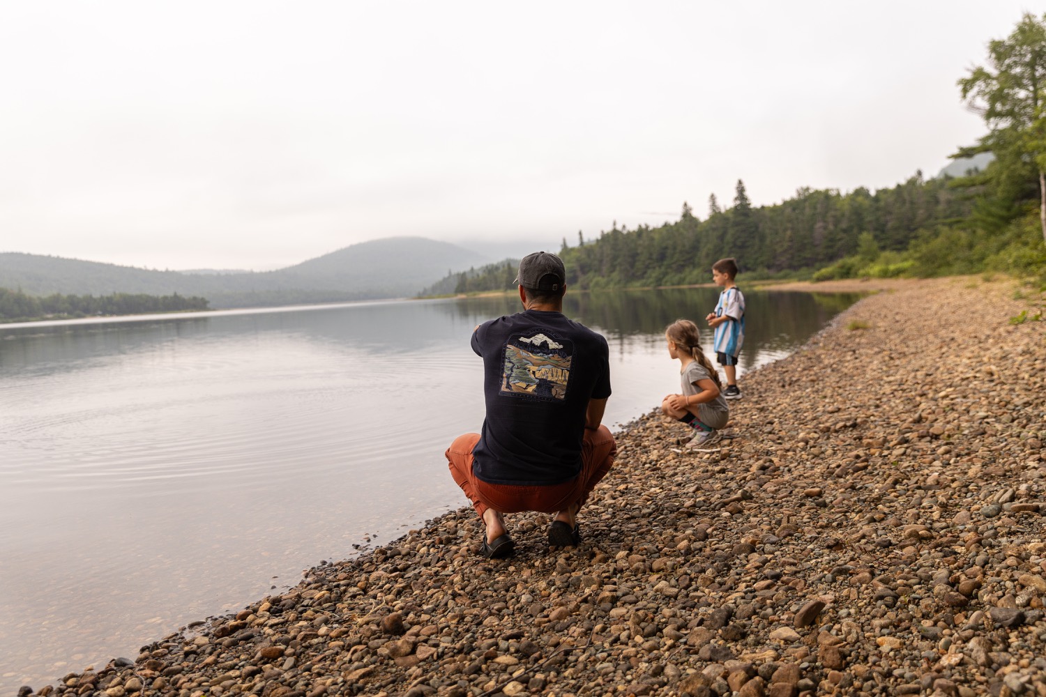 A father crouched at the edge of a misty lake with his two kids at a DrivenDad retreat